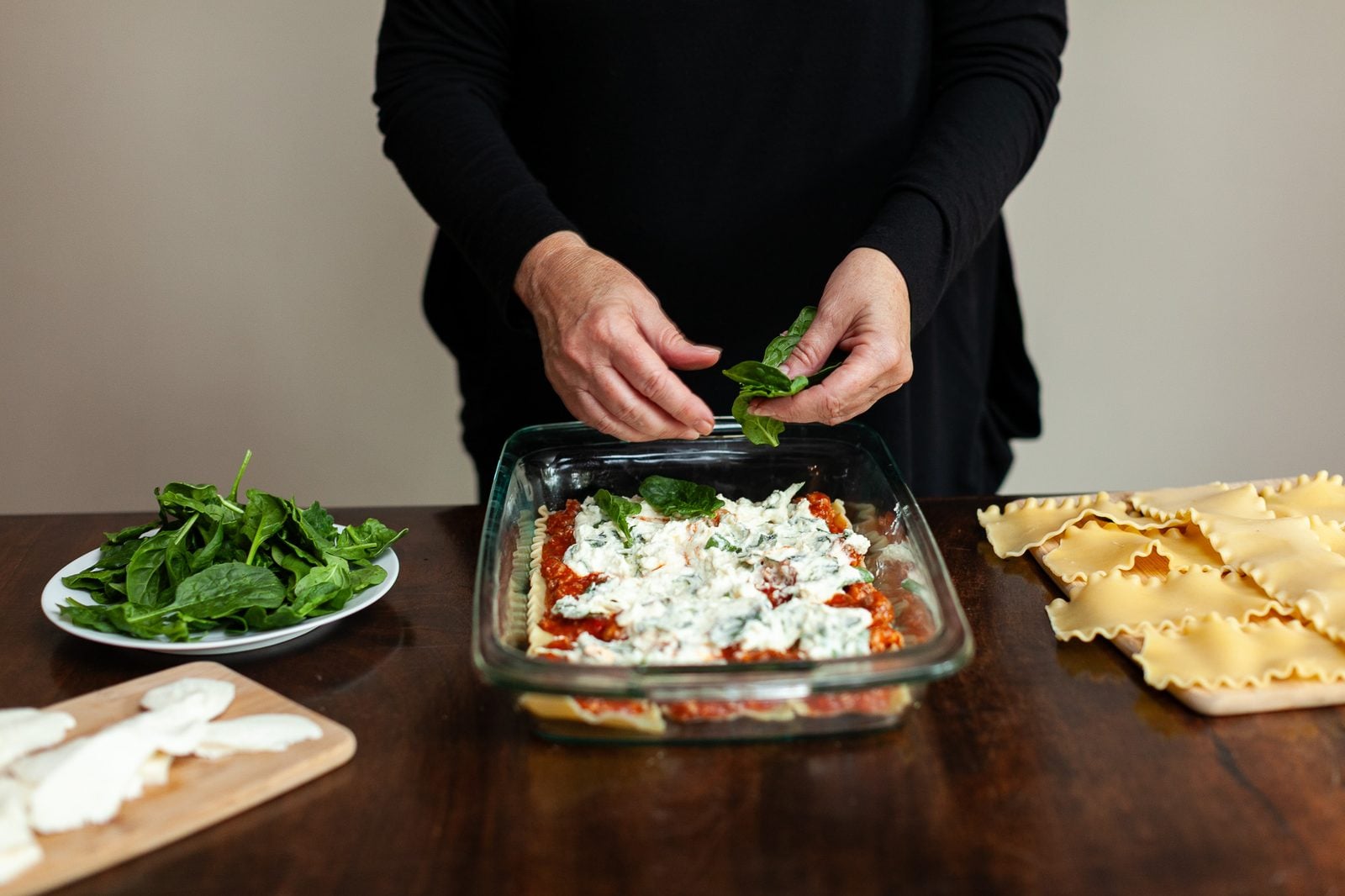 Photo (not an illustration) of a thick slice of lasagna on a plain plate indoors, showing distinct layers of pasta, red sauce, and ricotta, with a fork nearby. No text or logos anywhere in the scene.